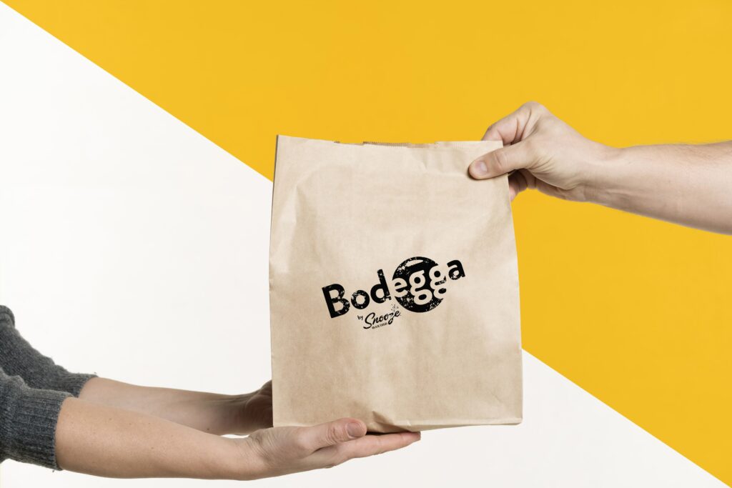 Two Hands Holding Brown Bag with Bodegga Logo